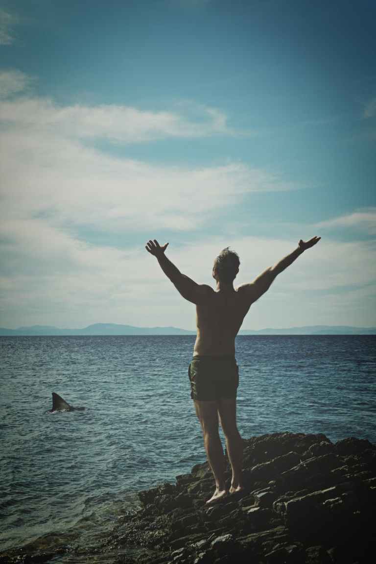 man standing on stone beside body of water during daytime