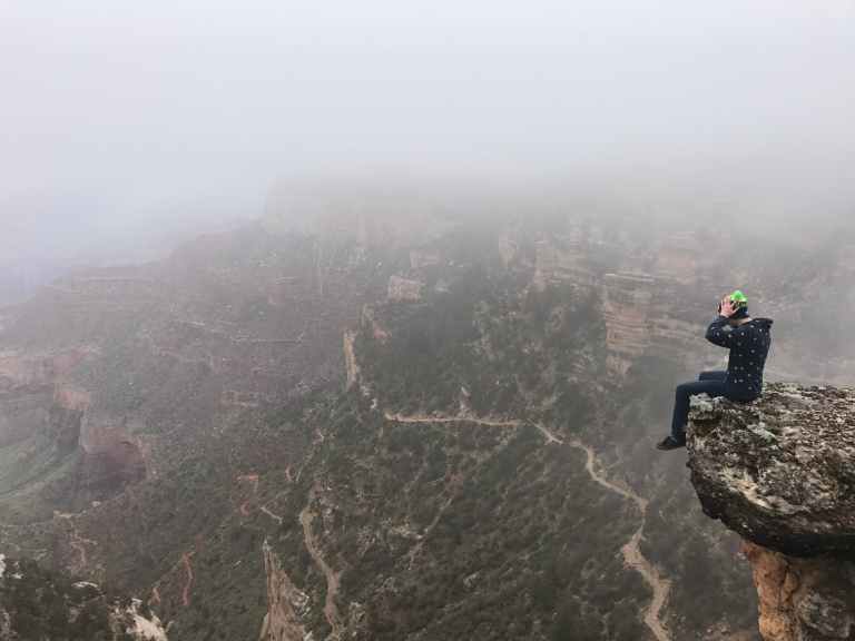 man sitting on top of cliff on foggy mountain
