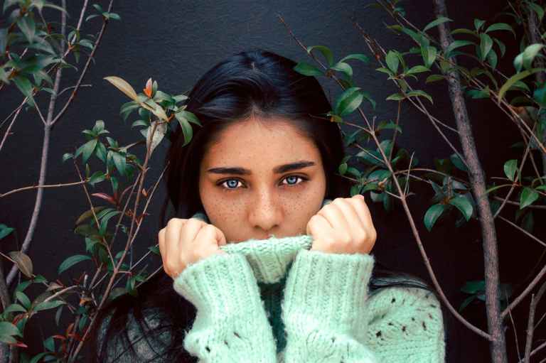 woman wearing knitted sweater besides green plants